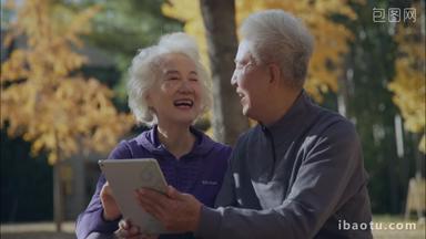 <strong>幸福</strong>的老年夫妇坐在户外看平板电脑